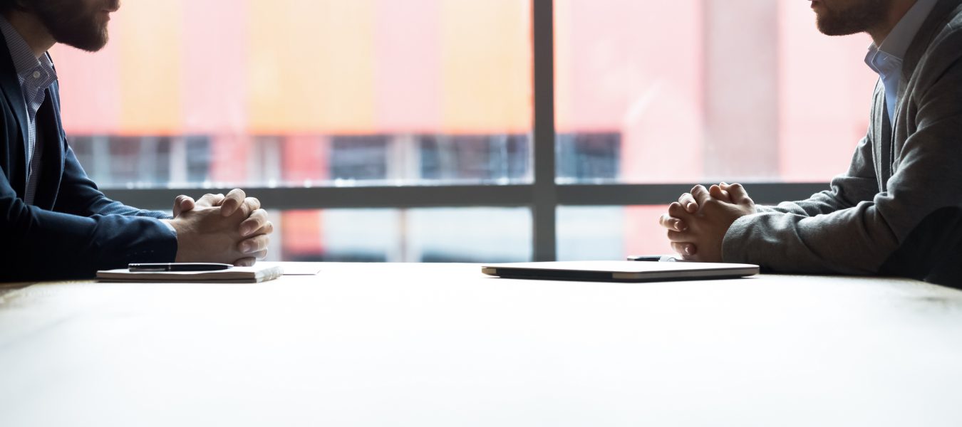 Side view two confident serious businessmen  with tensed nerves sit at boardroom desk looking at each other, rivalry bad attitude, confrontation during difficult negotiation, leadership tussle concept